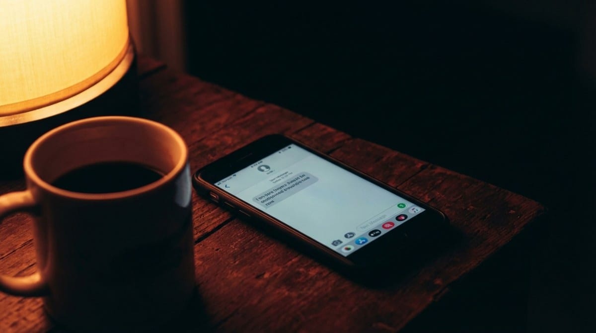Close-up of phone showing a short text message next to a cup of coffee in a dimly lit setting