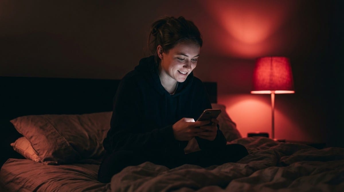 Woman smiling while texting on phone at night in bedroom