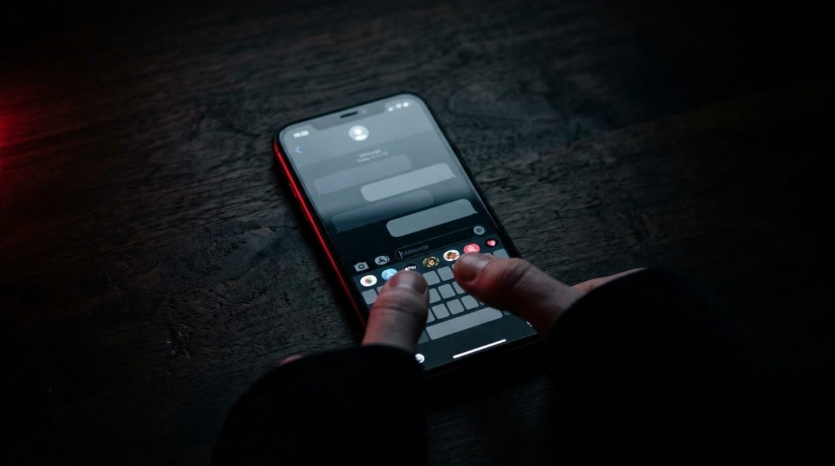 Close-up of hands typing a message on a smartphone in a dark environment with minimal lighting
