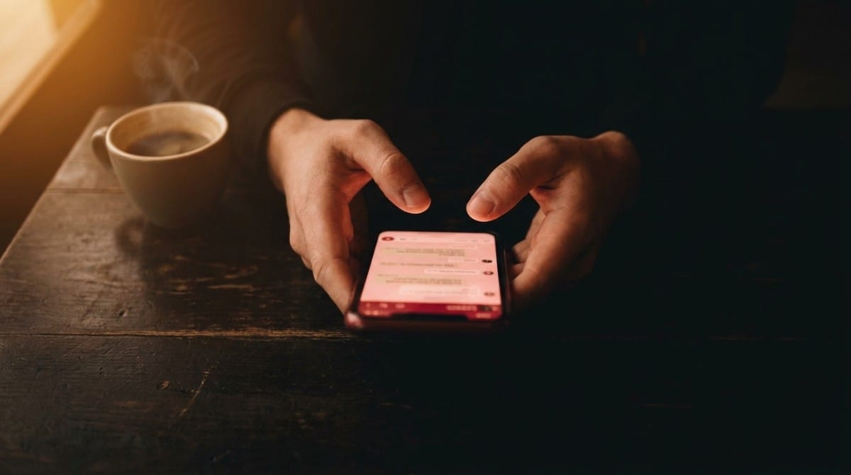 Close-up of hands texting on a smartphone beside a cup of coffee in dim lighting, representing late-night conversations and digital intimacy