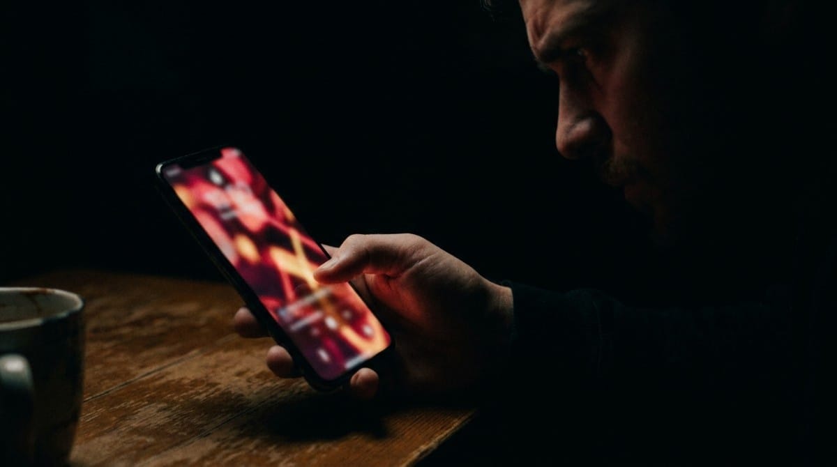 Close-up of a person studying a smartphone screen in a dark setting, highlighting intense focus, over analysis, and emotional uncertainty around digital communication.