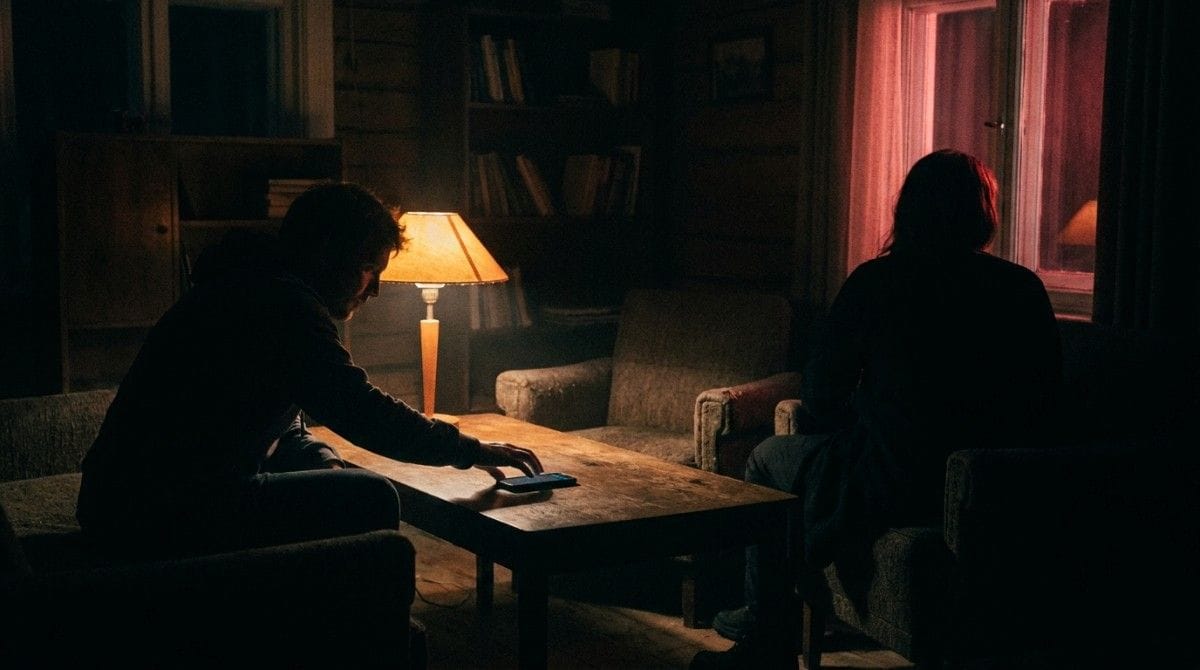 Two people sitting apart in a dimly lit room, creating a sense of emotional distance and tension.