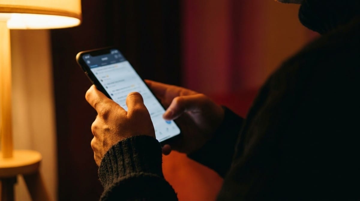 Close-up of hands holding a smartphone while reading messages in a dimly lit room.