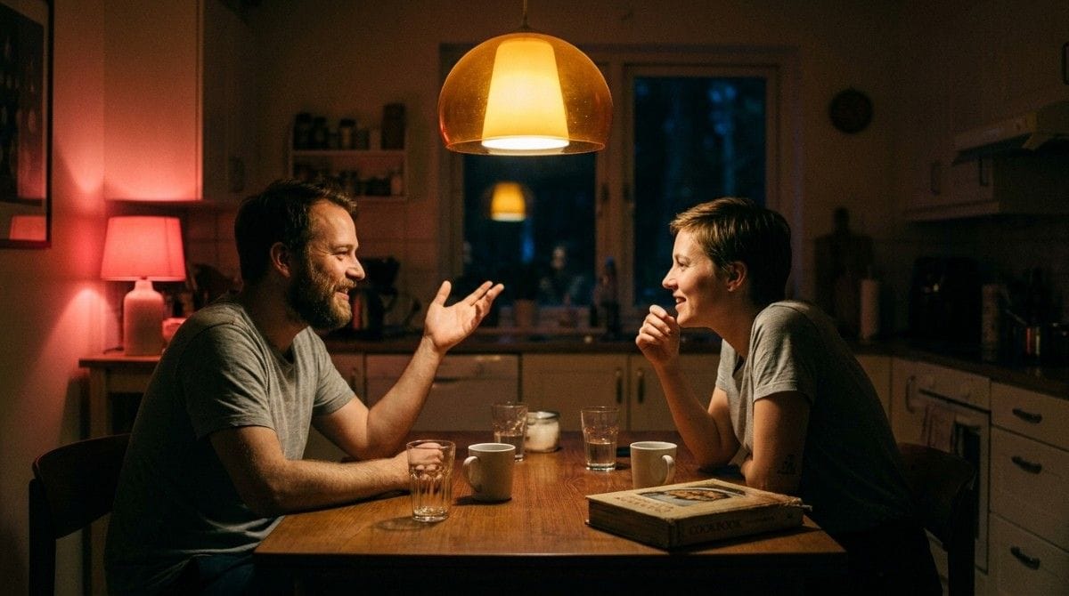 Two people talking and smiling across a kitchen table during a cozy evening conversation at home.