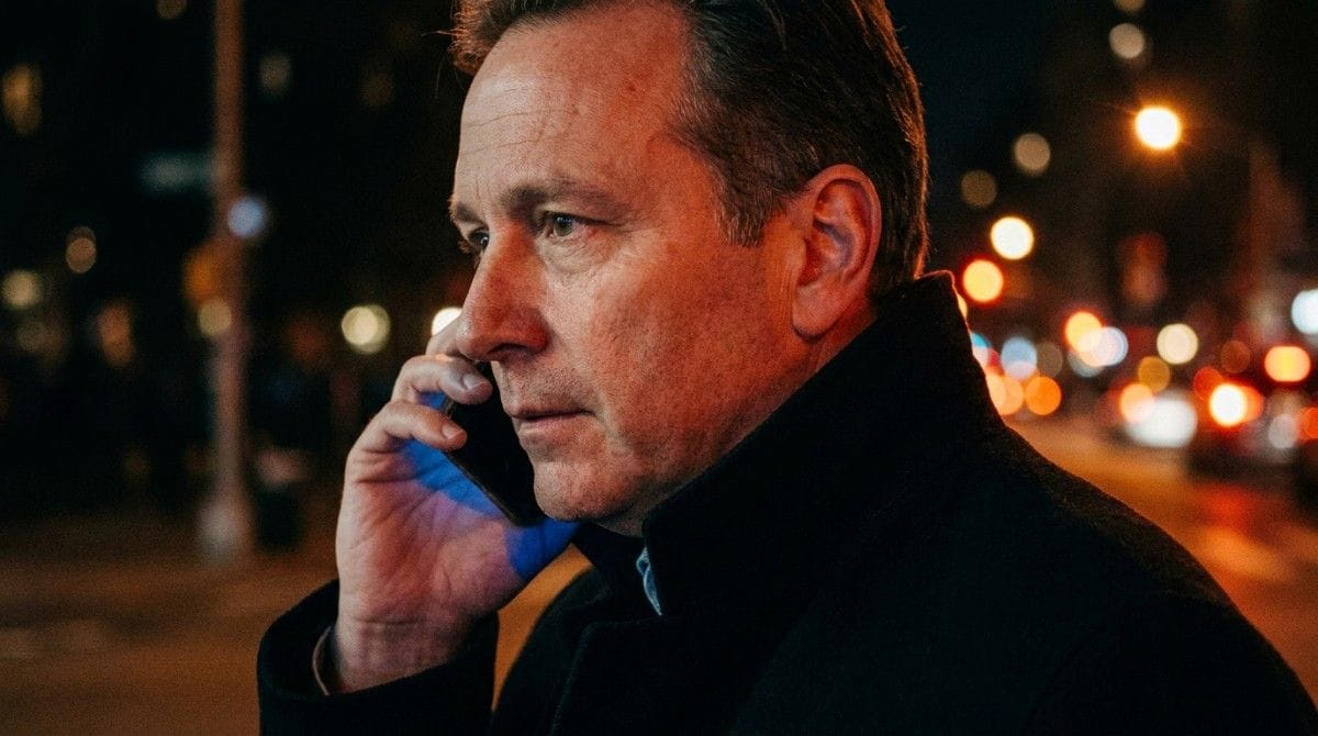 Man talking on a smartphone while standing outdoors at night with city lights in the background.